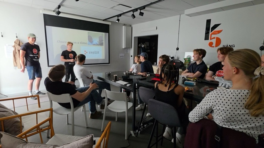 Workshop room with presenters and young participants around a long table and a projected slide